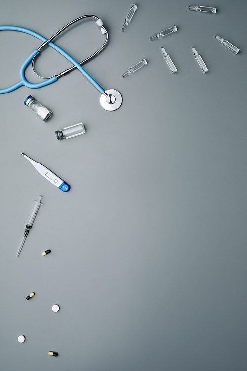 Minimal composition of medical equipment with antibiotics and stethoscope laid out over grey background, copy space