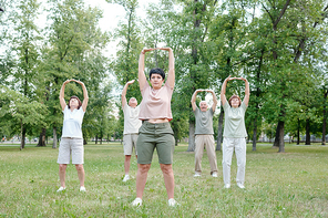 Group of senior people and their coach raising arms up while stretching body at outdoor fitness class