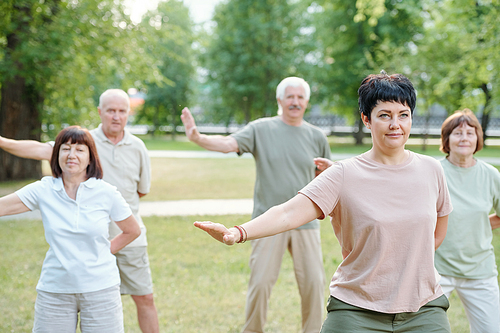 Active mature people standing in park and moving arms at qigong practice