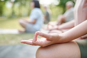 Close-up of unrecognizable woman touching fingers in mudra while meditating at group class outdoors