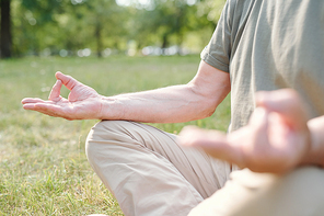 Close-up of unrecognizable woman holding hands in mudra and meditating in half lotus pose while practicing yoga outdoors