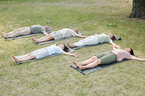 Group of mature yoga students lying in corpse pose on mats while resting after training in park