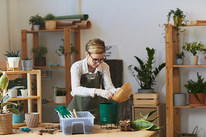 Waist up portrait of young woman putting fresh soil into pot while caring for houseplants indoors, copy space