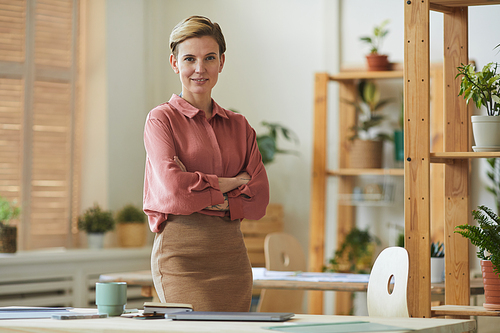 Waist up portrait of successful businesswoman  while standing with arms crossed in office interior decorated with plants, copy space