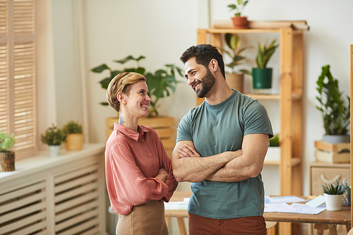 Waist up portrait of two young colleagues smiling cheerfully while chatting in office, copy space