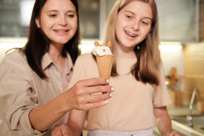 Happy young woman showing yummy homemade icecream in waffle cone decorated by her teenage daughter with almond nuts
