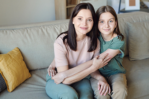 Portrait of content brunette mother sitting on sofa and hugging teenage daughter at home