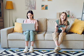 Concentrated mother using laptop and working at home while her daughter playing video game