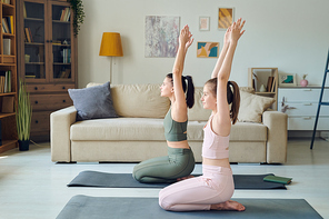 Mother and teenage daughter sitting on exercise mats and practicing yoga at home
