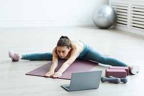 Minimal full length portrait of fit young woman doing splits and stretching while enjoying workout at home in white room, copy space