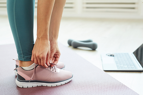 Side view close up of fit young woman tying shoe laces while standing on yoga mat ready for online workout at home, copy space