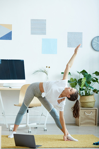 Vertical full length portrait of contemporary young woman warming up and stretching during fitness workout at home, copy space