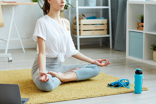 Cropped portrait of contemporary young woman doing yoga while sitting in lotus position during home workout, copy space