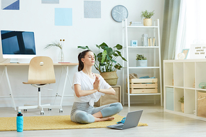 Full length portrait of contemporary young woman doing yoga while sitting in lotus position at home, copy space