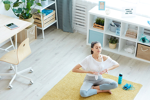 Wide angle view at modern young woman enjoying breathing exercises while meditating at home, copy space