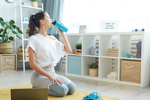 Full length portrait of modern young woman drinking water after home workout, copy space