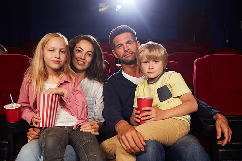 Front view portrait of happy family with two kids  while waiting to watch movie in cinema theater