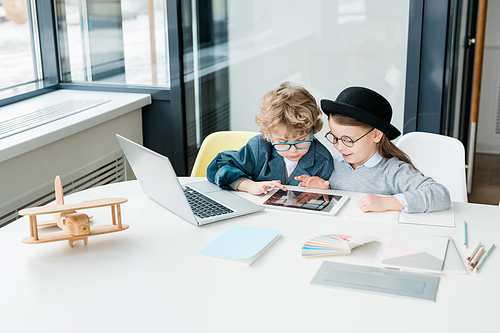 Cute elementary school friends with digital tablet scrolling through online information in classroom at lesson