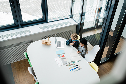 Two cute little designers consulting about online data while preparing new creative project by classroom window