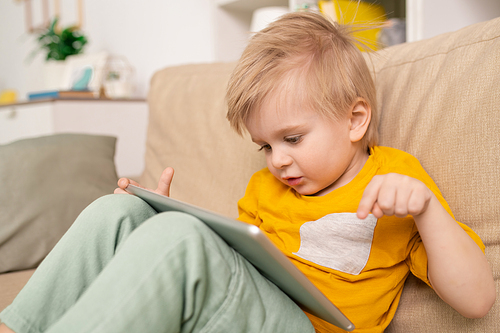 Close-up of cute boy sitting on sofa and talking to parent via telecommunication app on tablet in living room