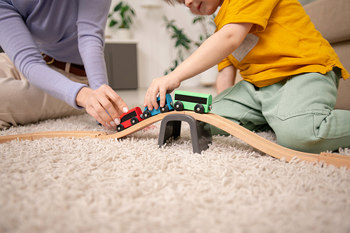 Close-up of mother and son sitting on carpet and playing with toy train on toy railway