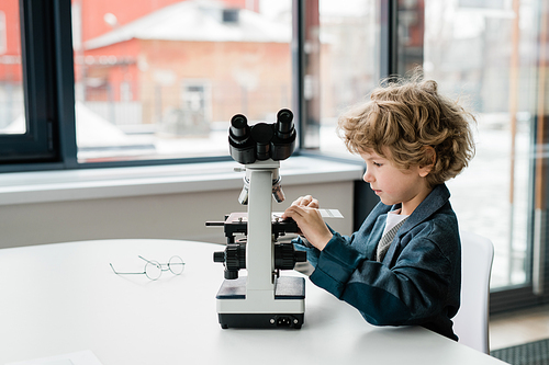 Clever little scientist putting chemical sample in microscope while going to study new elements in laboratory
