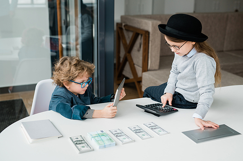 Two adorable economists of elementary age making calculations and financial analysis during working meeting in office