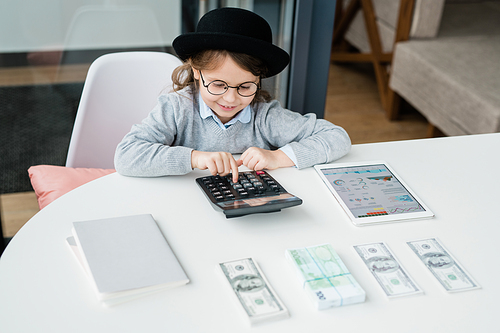 Little accountant using calculator while counting salary or money and making financial analysis by desk