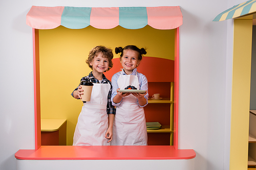 Cute little girl and boy giving you glass of drink and plate with berry cake or dessert while working in school cafeteria