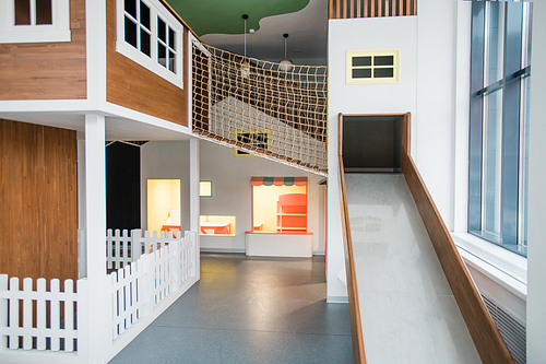 Interior of contemporary children leisure center with slide, small house and net between them on play area