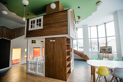 Play area with slide, small house and table with chairs around and lamps above inside contemporary leisure center