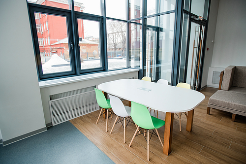 White desk with group of colorful chairs around standing by window inside contemporary leisure center for children