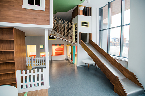 Play area with slide, small house and net between them inside contemporary leisure center for children