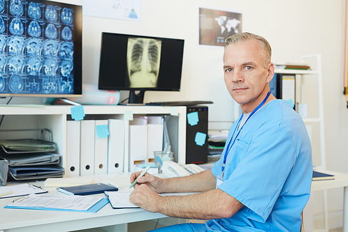 Portrait of handsome mature doctor  while posing at workplace in modern clinic interior with CT scans in background, copy space