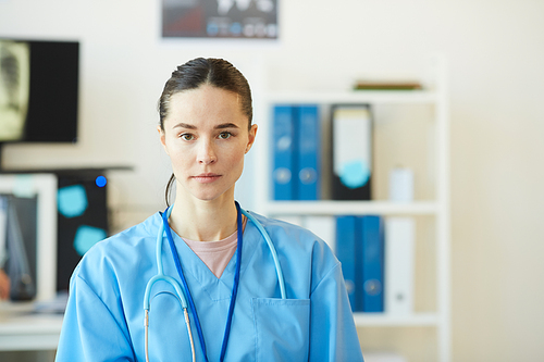 Portrait of adult female medic wearing blue uniform  while standing in clinic interior, copy space