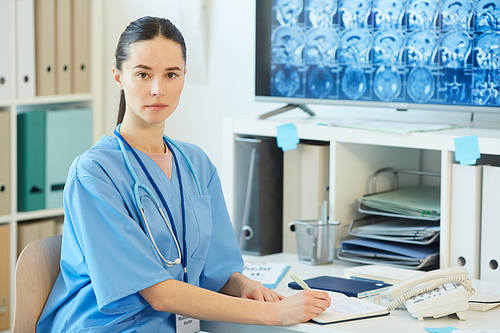 Waist up portrait of adult female doctor  while posing at workplace with CT scans in background, copy space