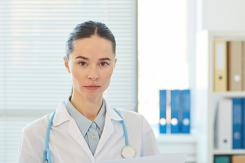Head and shoulders portrait of serious female doctor  while sitting at workplace in modern clinic, copy space