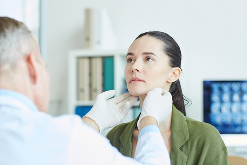 Portrait of unrecognizable doctor palpating neck while examining young woman during consultation in clinic or hospital, copy space