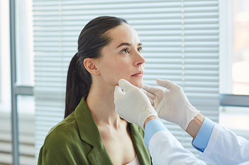 Side view of unrecognizable doctor palpating neck while examining young woman during consultation in clinic or hospital, copy space