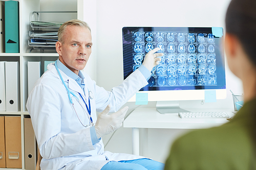 Portrait of handsome mature doctor pointing at brain scan images while consulting young woman in modern neurology clinic, copy space