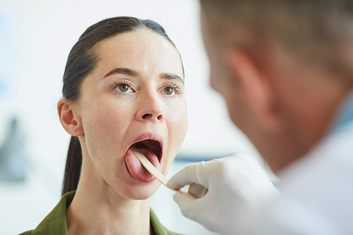 Close up portrait of young woman opening mouth during throat examination in clinic, copy space