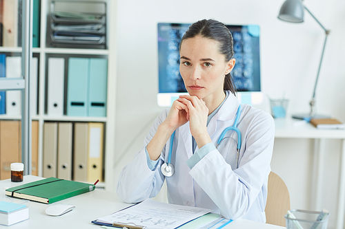 Portrait of serious female doctor  while sitting at desk in office of modern clinic, copy space