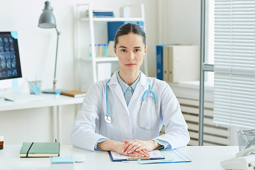 Portrait of professional female doctor  while sitting at desk in office of modern clinic, copy space