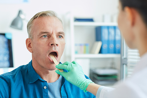Close up portrait of mature man opening mouth during throat examination in clinic, copy space