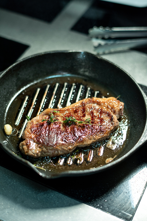 Appetizing roasted beef steak seasoned with fresh aromatic herbs on grill frying pan standing on electric stove in the kitchen of modern restaurant
