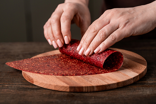 Hands of creative housewife rolling homemade fruit leather on wooden board by kitchen table while making tasty and healthy food