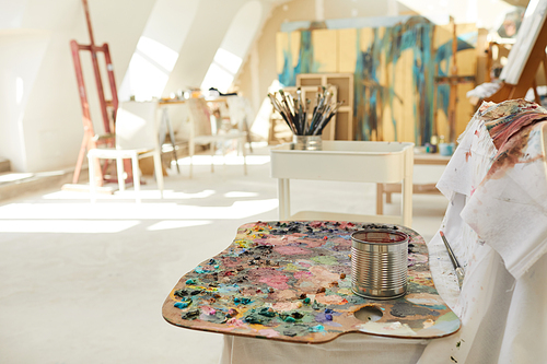 Background image of empty art studio lit by sunlight, focus on artist pallet in foreground, copy space