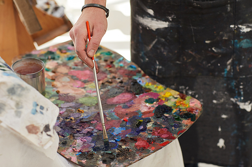 Close up of unrecognizable male artist mixing paint on palette while painting in art studio, copy space