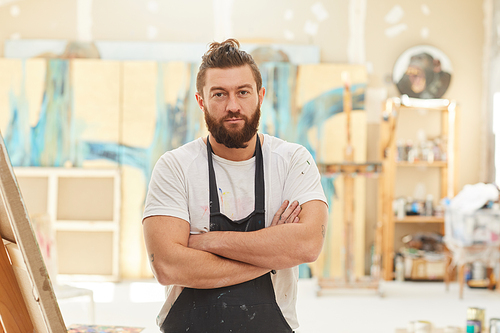 Waist up portrait of mature bearded artist standing with arms crossed and  while posing in spacious art studio lit by sunlight, copy space