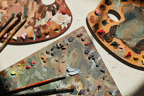 Top down view at artists palettes splattered with paint lying on table lit by sunlight, minimal background image, copy space